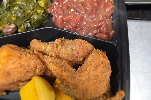 An image of a soul food plate with red beans and rice, greens, fried chicken, and cornbread