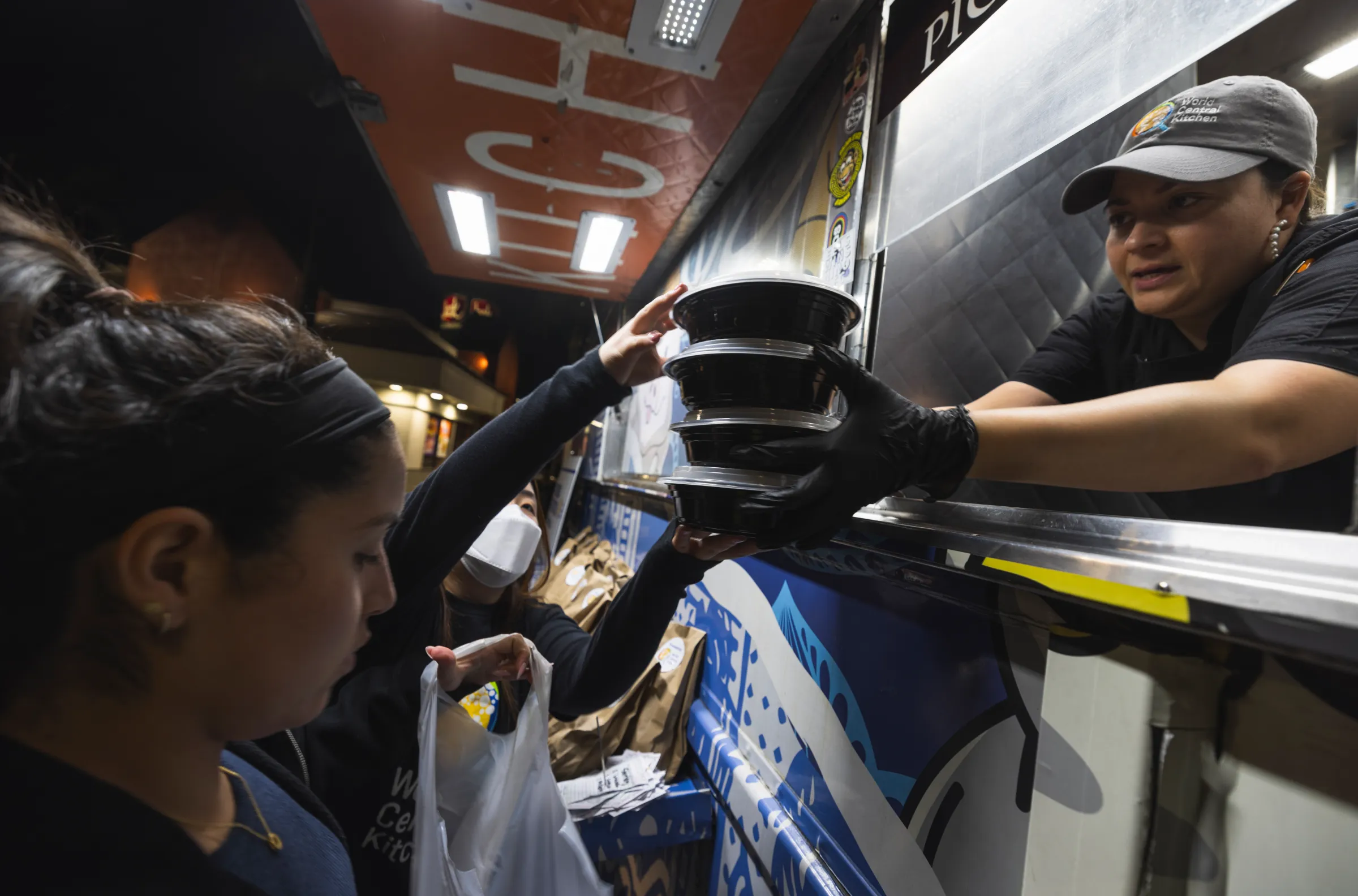 And image of a woman in a food truck serving at least four take out containers of food to a customer.
